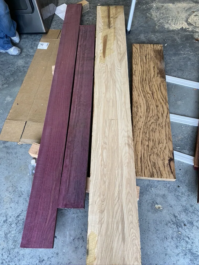 Rough purpleheart, ash, and zebrawood boards laid out before milling